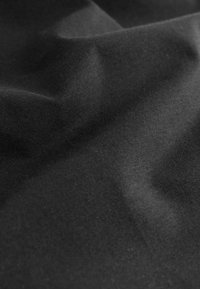 Tissu noir avec des plis doux et une surface lisse légèrement texturée, présenté en gros plan.