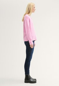 Rosa stickad tröja med ribbad nederkant, tillsammans med mörkblå skinny jeans och svarta ankboots med tjocka sulor.