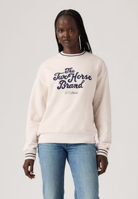 Lichtbeige sweatshirt van zacht stof met marineblauwe borduursels van "The Two Horse Brand," aangevuld met gestreepte manchetten.