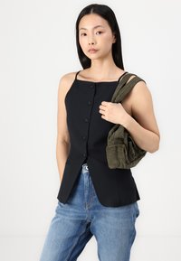 Černý top bez rukávů s knoflíkovou přední částí, přizpůsobený design a mírný peplum. Kombinováno se světle modrými džíny a olivově zelenou texturovanou taškou.