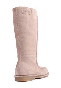 Stivale alto in suede beige con punta rotonda, texture liscia, dettagli di cuciture sottili e una toppa con logo marrone in cima. Suola piatta beige.