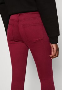 Bordeaux jeans met een aansluitend ontwerp, een gladde textuur, twee achterzakken en stiksels. De tailleband is hoog.
