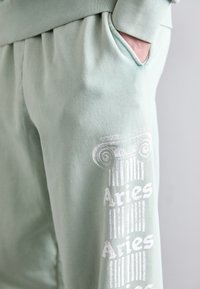 Mintgrønne sweatpants med en sidelomme, prydet med hvide trykte søjler og tekstaccenter. Lavet af blødt stof med en glat tekstur.