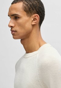 Helle beigefarbene, gerippte Strickjacke mit Rundhalsausschnitt und strukturiertem Gewebe mit dezenten horizontalen Linien. Eng anliegende Silhouette.