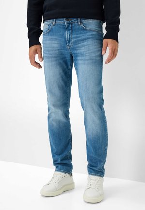 Jean en denim bleu clair avec une coupe droite, finition décolorée et légère patine. Associés à des baskets blanches.