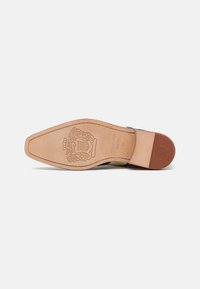 Suola della scarpa con una finitura in pelle liscia color cammello, forma appuntita, dettaglio logo impresso e un leggero tacco per un'elevazione aggiuntiva.