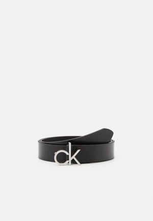 Ceinture en cuir noir roulée à plat avec une boucle logo "ck" en argent sur un fond clair uni.