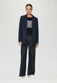 Námornícky blazer cez pruhovaný námornícky a biely sveter, spárovaný s tmavými širokými džínsy a bielymi teniskami. Hladká tkanina, štruktúrovaný dizajn.