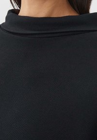 Černá, texturovaná tkanina s vysokým, skládacím límcem. Detailní záběr ukazující žebrované detaily a hladký povrch.