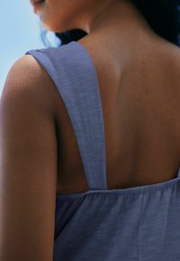 Lavendelfarbenes ärmelloses Oberteil mit breiten Trägern, das eine glatte Textur und einen leichten Glanz aufweist und den Bereich der Schulter und des Nackens zeigt.