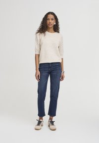 Pull en maille beige clair avec des manches courtes texturées, associé à un jean délavé foncé et des baskets crème avec des accents noirs. Présentation d'une tenue décontractée.
