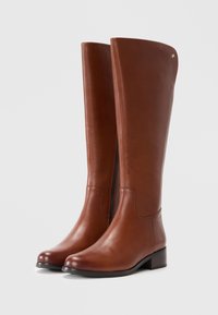 Brown leather knee-high boots with a side zipper, rounded toe, and a low block heel. Smooth texture with minimalistic design accents.
