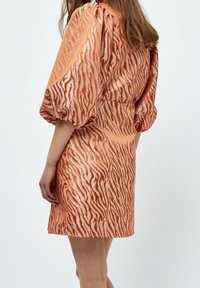 Kortärmad klänning i orange och krämfärgad zebramönster, med en figurnära midja och mjuk, texturerad tyg. Informell längd.