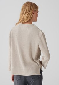 Helles, beiges, ribbed Langarmoberteil mit weitem Ausschnitt, seitlichen Schlitzen und lockerer Passform. Der Stoff hat eine strukturierte Optik.