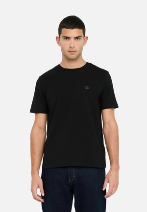 T-shirt nera in cotone a girocollo con maniche corte, caratterizzata da un logo discreto sul petto. Abbinata a jeans in denim scuro.