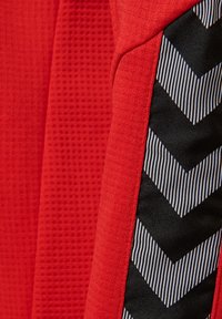 Close-up af rødt stof med vaffeltekstur ved siden af et sort-hvidt chevronmønstret vævet bånd.