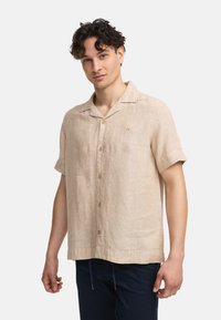 Camisa de lino beige de manga corta con un cuello de campamento, botonadura frontal y una textura sutil. Presenta un pequeño logotipo bordado en el pecho.