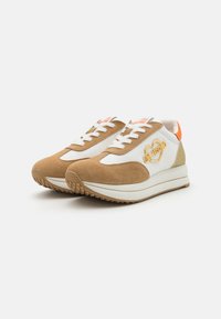 Brown suede and white leather sneakers feature a golden heart logo, orange heel accent, and white laces. Textured rubber sole for grip.