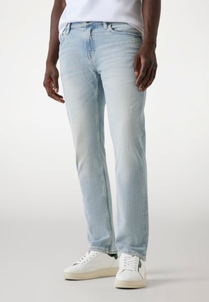 Lichtblauwe denim jeans met een rechte pasvorm, met subtiele vervaging en slijtage, gecombineerd met witte sneakers op een neutrale achtergrond.