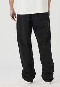 Črne kavbojke iz jeansa z ohlapnim krojem, ravnimi hlačnicami, dvema zadnjima žepoma in minimalističnimi šivi, kombinirane z belimi supergami.