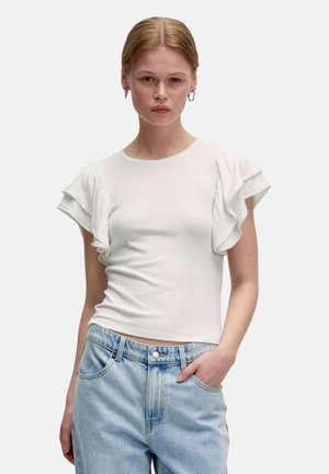 Witte geribbelde t-shirt met korte, gerimpelde mouwen. Eenvoudige ronde hals. Draagt met lichtblauwe high-waisted jeans, met zakken.