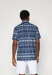 Camicia a maniche corte di colore blu navy con motivi di palme bianche e design geometrici. Presenta un colletto a button-down e una vestibilità comoda.