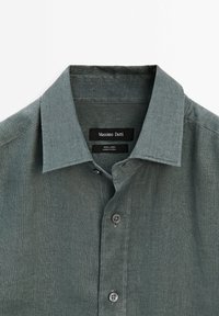 Chemise en lin gris-vert avec col et boutons, étiquette de marque visible Massimo Dutti et étiquette en tissu indiquant 100 % lin, fabriquée en Chine.