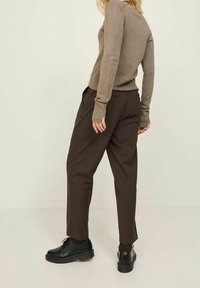 Brun långärmad tröja och mörkbruna byxor med en avslappnad passform. Svarta skor med en robust sula. Slät tygtextur.