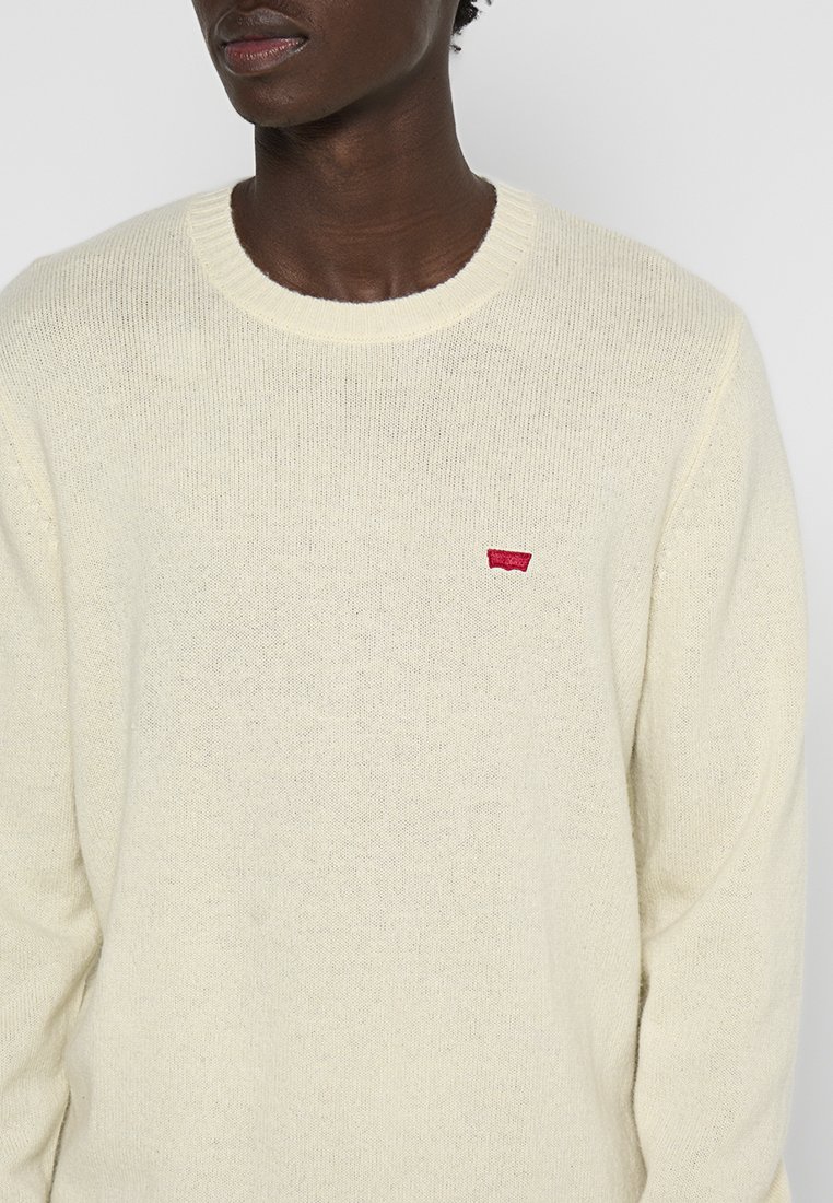 Maglione color crema con finitura testurizzata, dotato di un collo rotondo e di un piccolo logo ricamato rosso sul lato sinistro del petto.