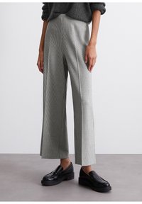 Grijs geruite wijde broek met een hoge taille, uitgevoerd in een textuurstof en met voorplooien. Gecombineerd met zwarte loafers.