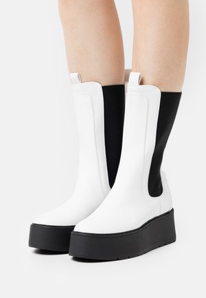 Botas de tornozelo brancas em plataforma com um design elegante, apresentando um acabamento brilhante e painéis laterais elásticos pretos para contraste.