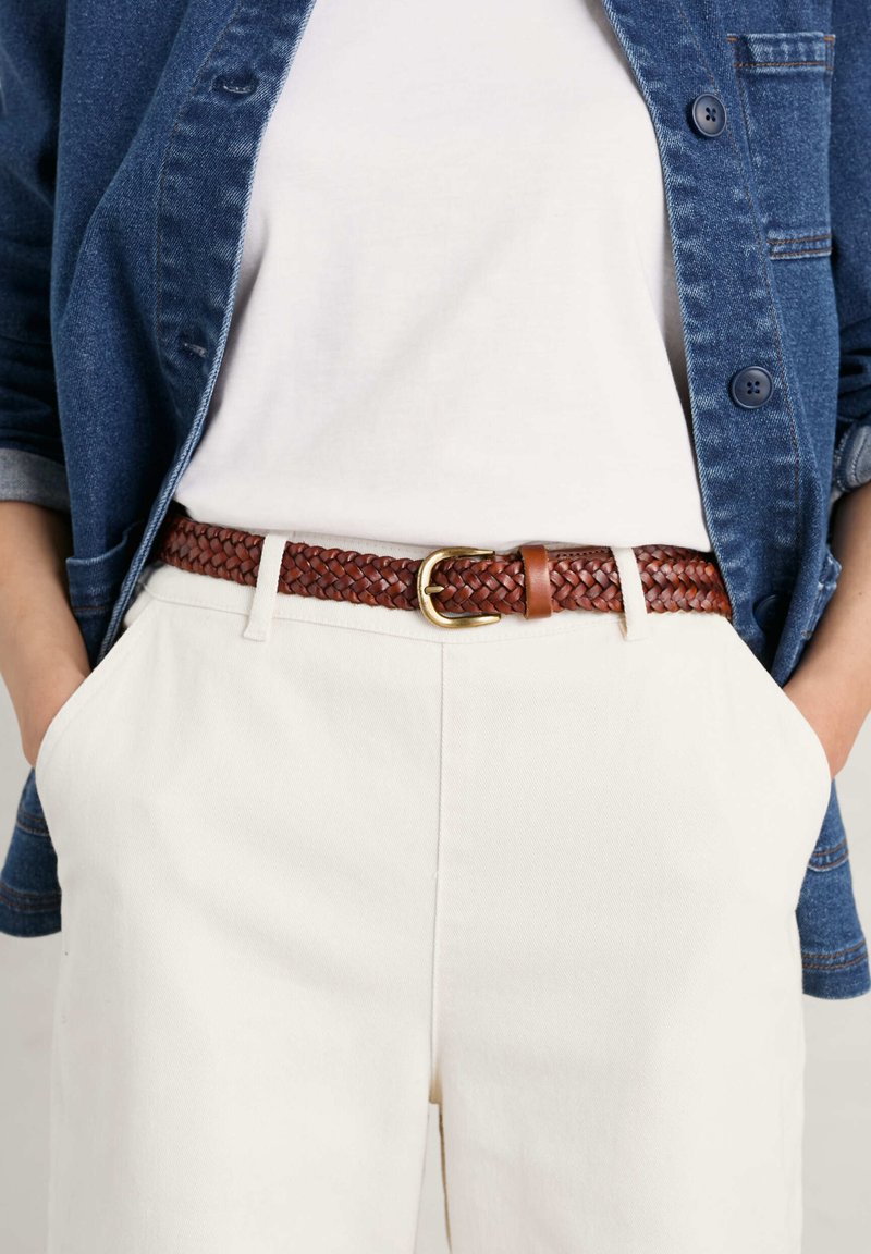 Vävd brun läderbälte med en guldspräng, bärs över vita byxor. Åtföljs av en blå denimjacka och en enfärgad vit topp.