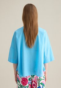 Top azul claro de manga corta con un corte holgado y una textura ligera. Combinado con una parte inferior de patrón floral colorido.