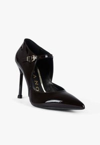 Scarpa con tacco alto in vernice marrone scuro lucida, caratterizzata da punta a punta e cinturino alla caviglia con una piccola fibbia argentata.