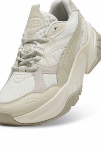 Baskets Puma beige et blanches avec des détails en mesh, suède et cuir, avec une semelle épaisse et des lacets.