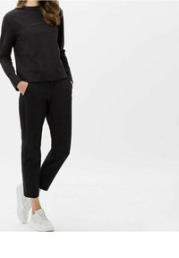 Sweatshirt noir et pantalon fuselé assorti en tissu doux. Baskets blanches et détail logo subtil sur le sweatshirt. Design minimaliste.