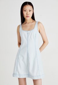 Light blue denim dress with a square neckline, thin straps, and flared skirt. Features stitched seams and a frayed hem detail.