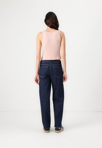 Top de tirantes rosa de canalé y corto, combinado con unos vaqueros de tiro alto de pierna ancha en azul oscuro y calzado negro con detalles blancos.