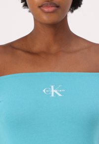 Türkiissinine õlgadelt avatud särk, mis on valmistatud pehmest puuvillasegust, millel on valge "Calvin Klein" logo ja sile, hästi istuv tekstuur.