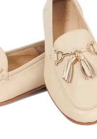 Beige leren loafers met een ronde neus, voorzien van een goudkleurige hardwaredetail en kwastjes op de voorkant. Glad, matte afwerking.