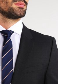 Marineblauwe blazer van een gestructureerde stof, slim fit, met notch-revers; gecombineerd met een witte overhemd en een blauwgestreepte das.