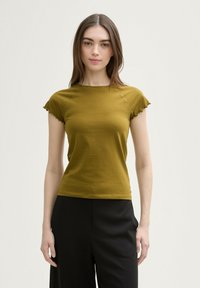 Top scurt de culoare verde măslinie, cu design ajustat, detalii cu cusături pe față și margini volan pe manșete; asortat cu pantaloni negri închiși.
