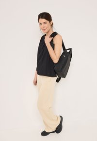 Black shoulder bag with adjustable strap; rectangular shape, smooth texture, subtle hardware details. Paired with a black top and beige pants.
