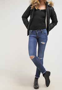 Black puffer jacket with fur trim over a fitted black top, paired with blue distressed skinny jeans and black ankle boots.