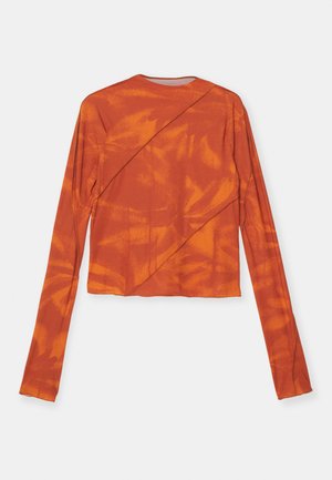 Long-sleeve top in burnt orange with a diagonal design. Smooth fabric with a slightly cropped cut and subtle abstract pattern across the surface.