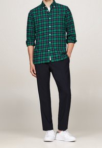 Groen en marineblauw geruit overhemd met een kraag, opgerolde mouwen, gecombineerd met marineblauwe broek en witte sneakers. Eenvoudig ontwerp, casual pasvorm.