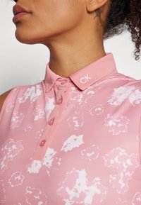Pink polo shirt with a textured floral pattern, featuring a button-up front and a collar branded with "CK." Soft fabric with a slight sheen.