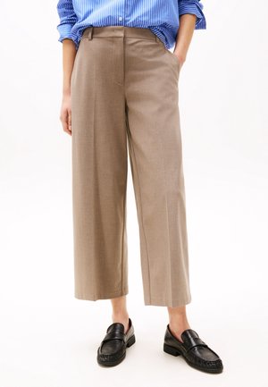 Persoon draagt beige wijde cropped broek met zwarte loafers en een blauw gestreept overhemd, hand in zak.