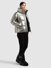 Sølvfarvet dunjakke med høj krave og lynlås, der har en skinnende overflade og sidelommer. Bådes med sorte leggings og snestøvler.