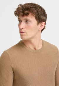 Suéter marrón de punto con cuello redondo. Tejido texturizado, diseño ajustado y remates acanalados en el cuello.